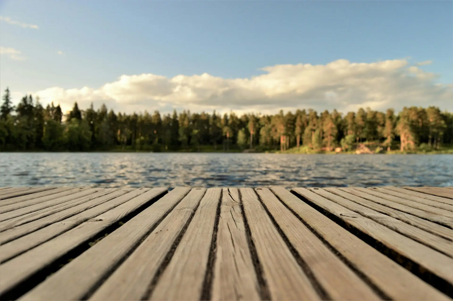 Serene wooden dock with a forested lake view under a bright summer sky in Sweden.